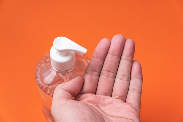 La mano del hombre en un recipiente con gel de alcohol en la pared de naranja