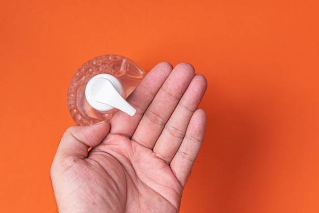 Foto gratuita la mano del hombre en un recipiente con gel de alcohol en la pared de naranja