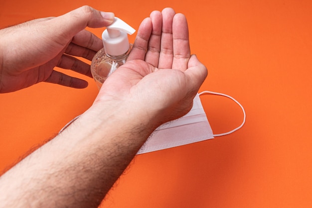 Foto gratuita la mano del hombre en un recipiente con gel de alcohol en la pared de naranja