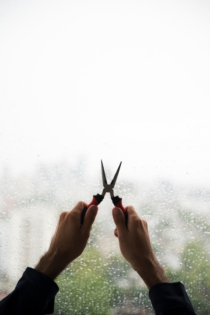 Mano del hombre sosteniendo alicates contra la ventana de gotas de agua