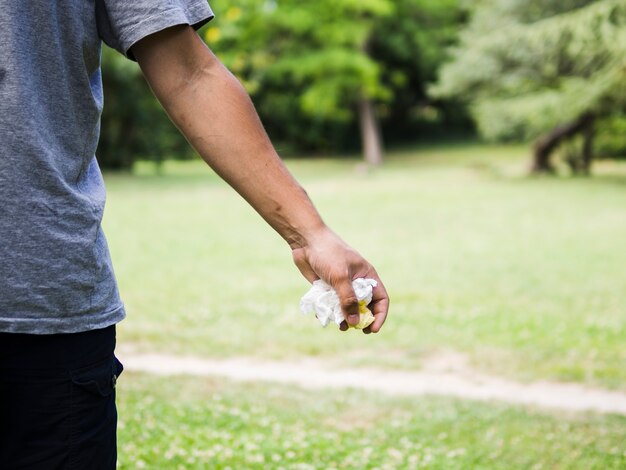 Mano de hombre sosteniendo papel arrugado en el parque