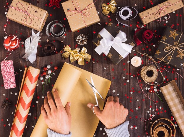 Mano de hombre sosteniendo un rollo de papel kraft con tijeras para cortar la caja de regalo de Navidad de embalaje