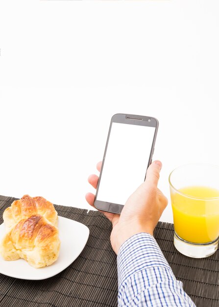 La mano del hombre sosteniendo smartphone con pantalla en blanco a la hora del desayuno