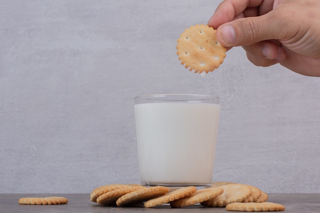 La mano del hombre sostiene una galleta encima de la leche en la mesa de mármol.