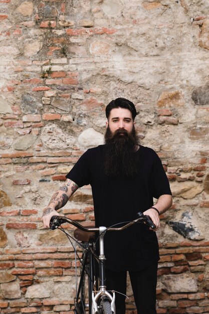 Mano del hombre con tatuaje en el asiento de la bicicleta contra la pared erosionada.