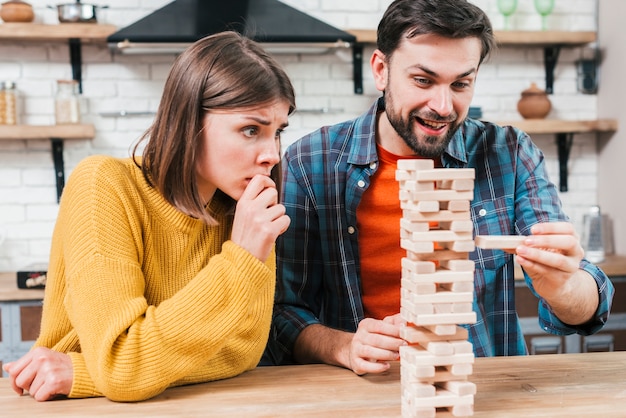 La mano del hombre tomando o poniendo un bloque a una torre inestable e incompleta de bloques de madera.