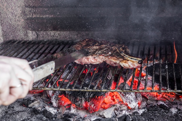 Mano humana asar carne en la parrilla de la barbacoa