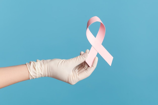 Mano humana en guantes quirúrgicos blancos shwoing y sosteniendo una cinta rosa, símbolo del cáncer de mama.