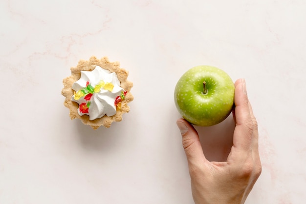 Mano humana sosteniendo manzana verde cerca de tarta de tarta sobre fondo