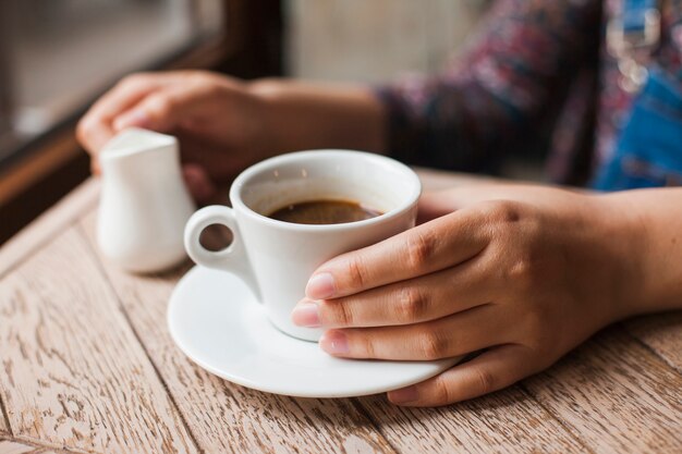 Mano humana sosteniendo la taza de café negro y jarra de leche