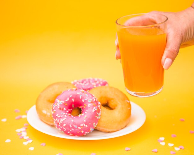 Mano humana sosteniendo un vaso de jugo cerca de donuts en un plato