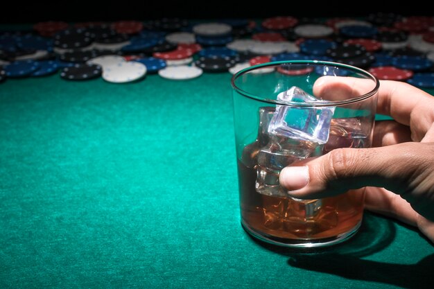 Mano humana sosteniendo el vaso de whisky en la mesa de póquer