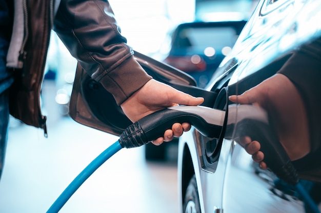 La mano humana sostiene la carga del automóvil eléctrico, conecte al automóvil