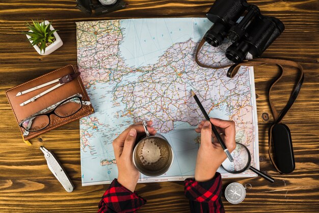 Mano humana con taza de café marcando destinos en el mapa