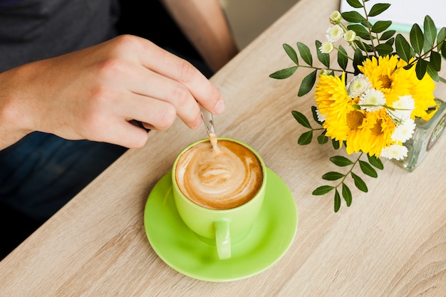 Mano humana usando una cuchara para revolver el café en la cafetería.