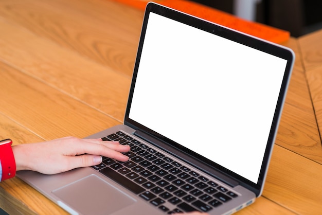 Mano humana usando laptop con pantalla blanca en blanco sobre escritorio de madera