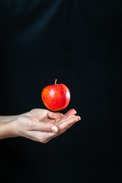 Mano humana vista frontal con una manzana en la oscuridad