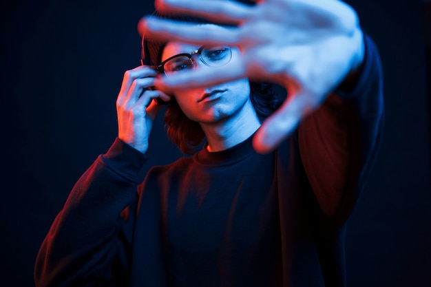 La mano izquierda está borrosa. Foto de estudio en estudio oscuro con luz de neón. Retrato de hombre serio