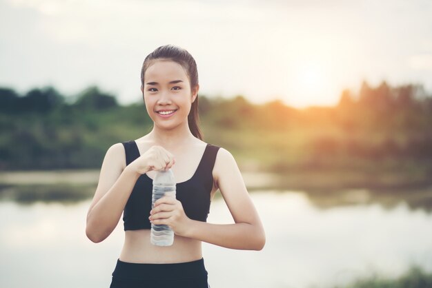 Mano joven de la aptitud de la mujer que sostiene la botella de agua después de correr el ejercicio