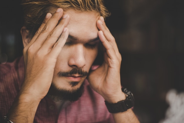 Foto gratuita la mano joven del hombre del inconformista en su cabeza mira seriamente a pensar mientras que se sienta en el café.