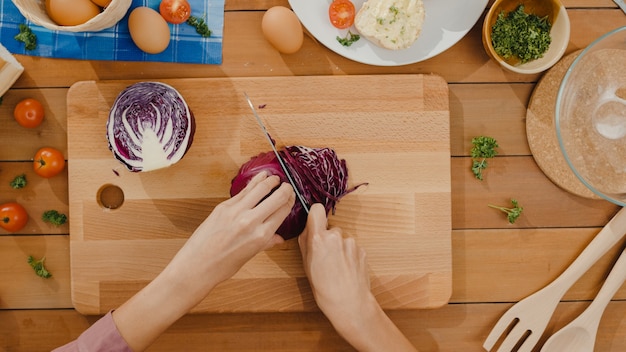 La mano de la joven mujer asiática chef mantenga la cuchilla cortando repollo rojo sobre tabla de madera
