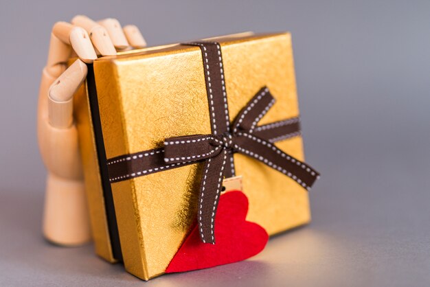 Mano de madera con caja de regalo con corazón