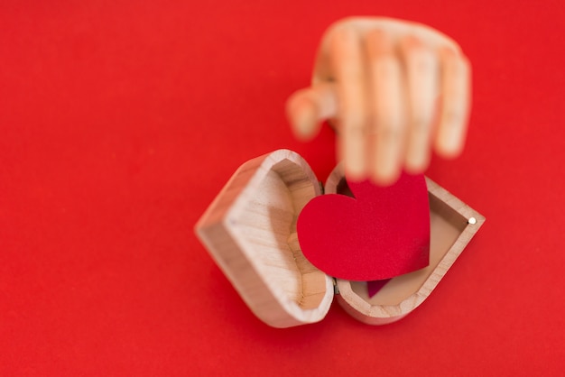 Mano de madera con corazón rojo en mesa roja