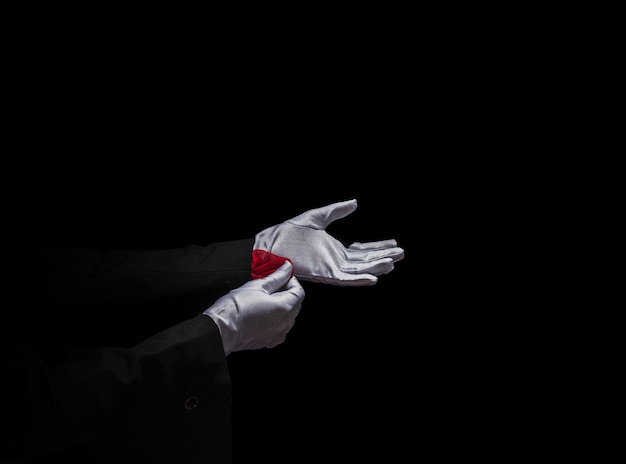Foto gratuita mano del mago que quita la servilleta roja de la manga contra fondo negro
