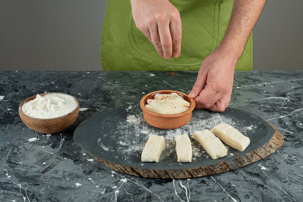 Mano masculina agregando sal a la masa en la mesa de mármol.