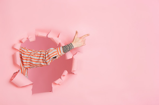 Foto gratuita mano masculina apuntando mostrando en copyspace de pared de agujero de papel de coral rasgado