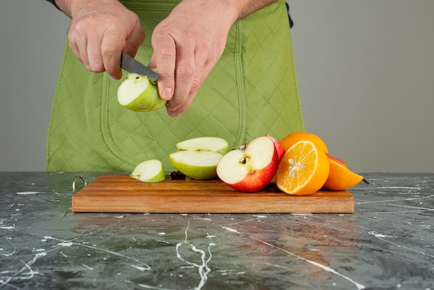 Mano masculina cortando manzana fresca en la parte superior de la tabla de madera en la mesa.