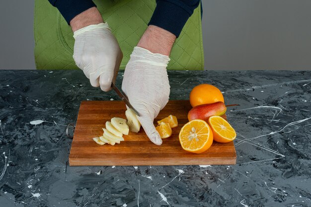 Mano masculina cortando manzana verde sobre mesa de mármol.