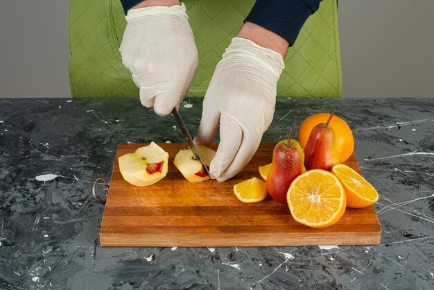 Mano masculina en guantes cortando manzana fresca sobre mesa de mármol.