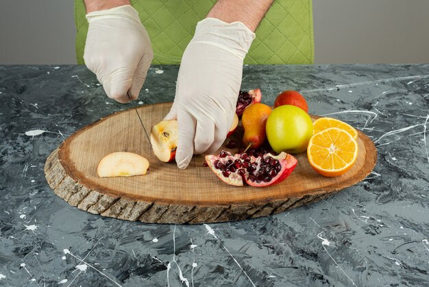 Mano masculina en guantes cortando manzana fresca sobre mesa de mármol.