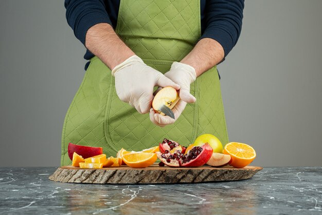 Mano masculina en guantes cortando manzana fresca sobre mesa de mármol.