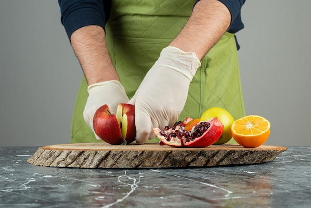 Mano masculina en guantes cortando manzana roja sobre mesa de mármol.