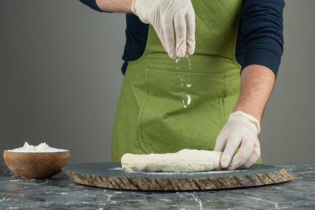 Mano masculina en guantes para hacer masa en la mesa de mármol.