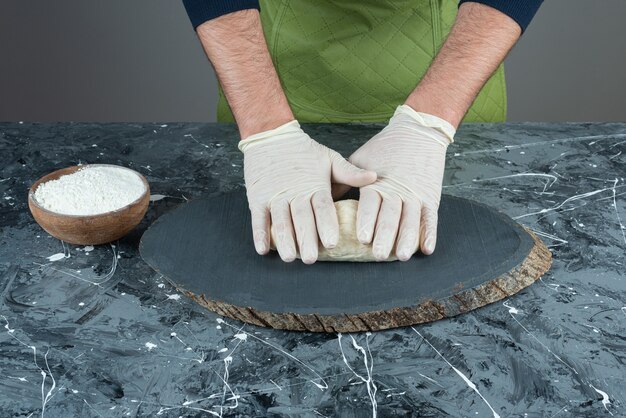 Mano masculina en guantes para hacer masa en la mesa de mármol.