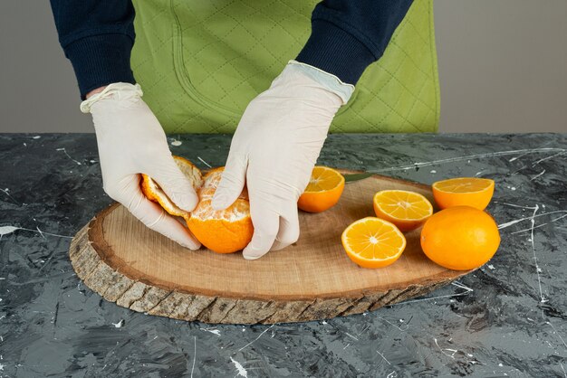 Mano masculina en guantes pelando mandarina fresca en la mesa.