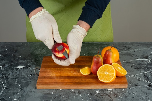 Foto gratuita mano masculina pelando la manzana roja en la parte superior de la tabla de madera en la mesa.