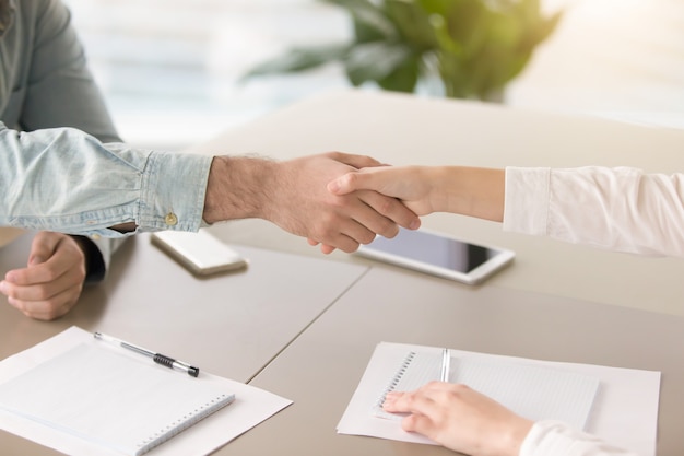 Mano masculina que sacude la mano de la hembra joven sobre el escritorio de oficina