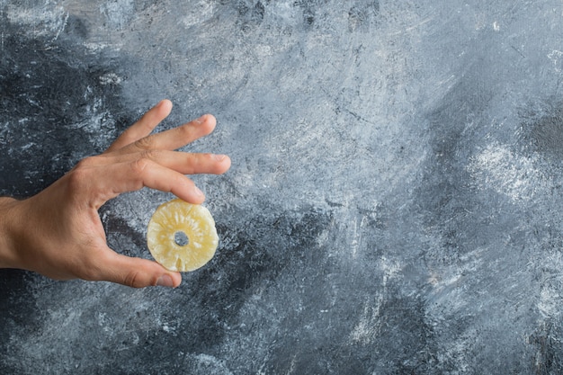 Mano masculina que sostiene el anillo de piña seca sobre fondo de mármol