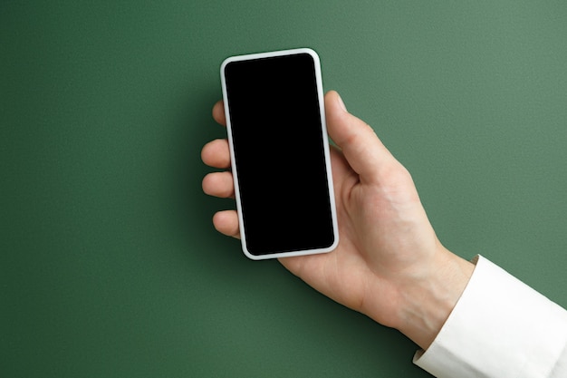 Mano masculina que sostiene el teléfono inteligente con pantalla vacía en verde