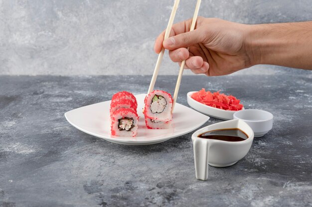 Mano masculina recogiendo sushi roll con palillos sobre fondo de mármol