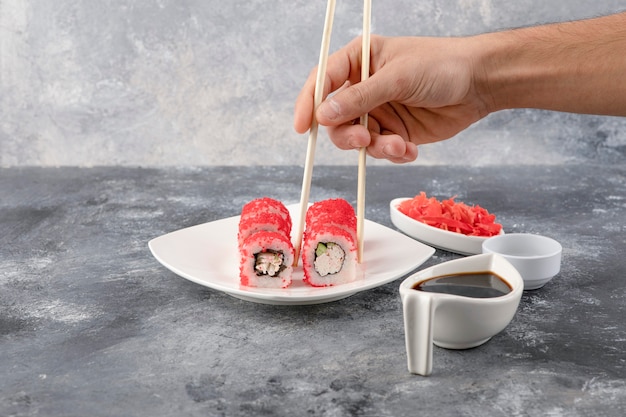 Mano masculina recogiendo sushi roll con palillos sobre fondo de mármol