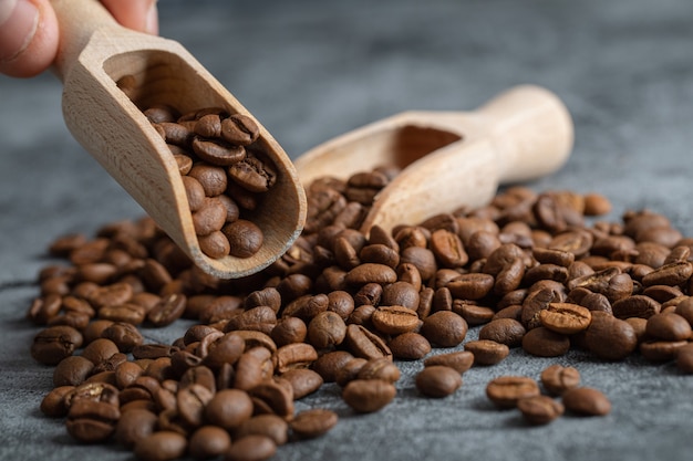 Mano masculina sosteniendo una cuchara de madera de aromáticos granos de café sobre fondo de mármol