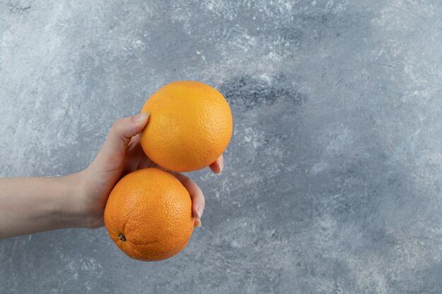 Mano masculina sosteniendo dos naranjas en la mesa de mármol.