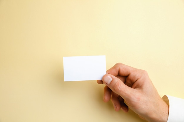 Mano masculina sosteniendo una tarjeta de visita en blanco sobre amarillo suave