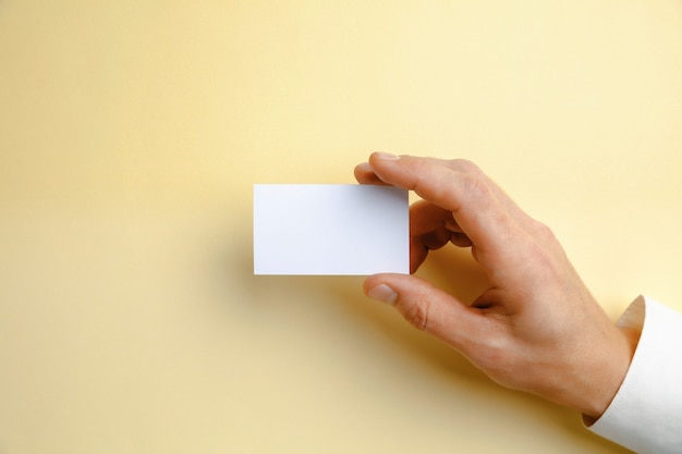 Mano masculina sosteniendo una tarjeta de visita en blanco sobre amarillo suave