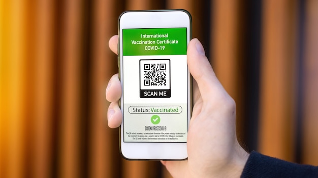 Mano masculina sosteniendo un teléfono inteligente con certificado de vacunación internacional código QR COVID19